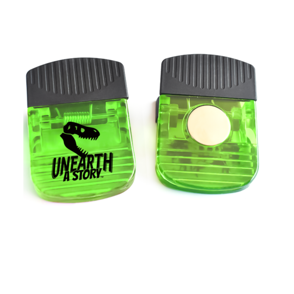 Two small translucent green magnetic clips shown front and back. One side features the “Unearth a Story” logo with a dinosaur skull, while the other shows a small round magnet.
