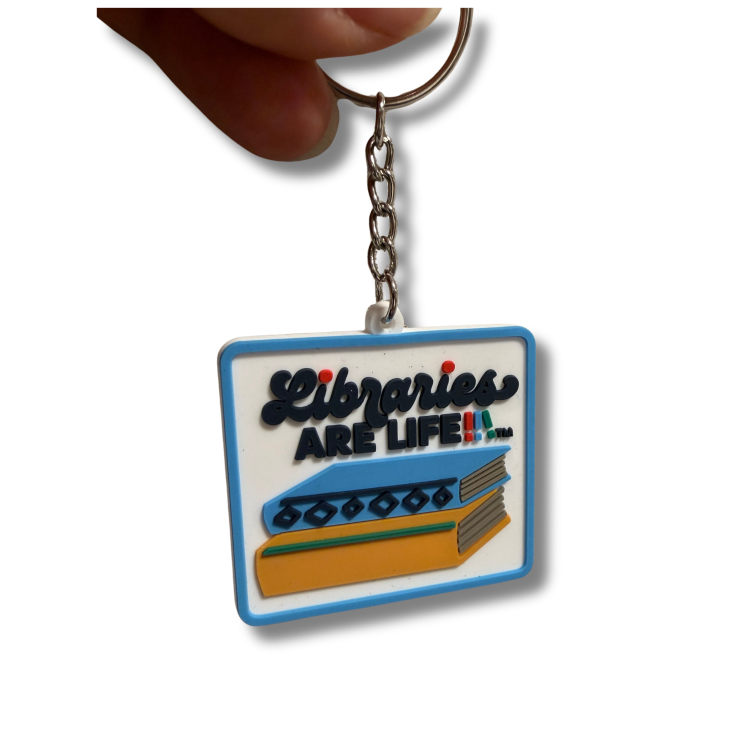 Close-up of a rectangular Libraries Are Life keychain featuring a white background, blue border, and raised lettering above a colorful stack of books. The design includes black text reading “Libraries Are Life” with small multicolored accents. A silver metal chain and split key ring are attached at the top.