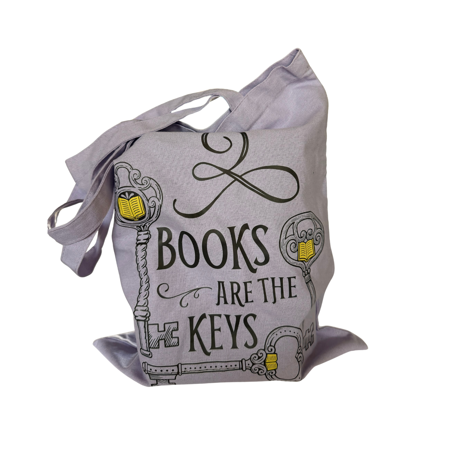 Lavender canvas tote bag with long shoulder straps, filled with books and featuring the phrase “Books Are the Keys” in black decorative lettering, surrounded by ornate skeleton key illustrations with yellow book accents, against a white background.