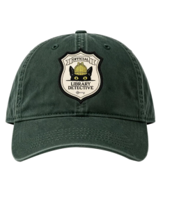 Dark forest green dad cap featuring a shield-shaped “Official Library Detective” patch with Inspector Whiskers, a black cat with yellow eyes wearing a detective hat.
