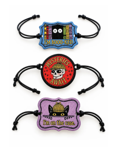 Three embroidered Mysteries Await adjustable wristbands with black cord straps on a white background. Designs include a blue “I’m Booo-ked” bookshelf with eyes, a red “Mysteries Await” detective skull, and a purple “I’m on the Case” featuring Inspector Whiskers in a yellow detective hat.
