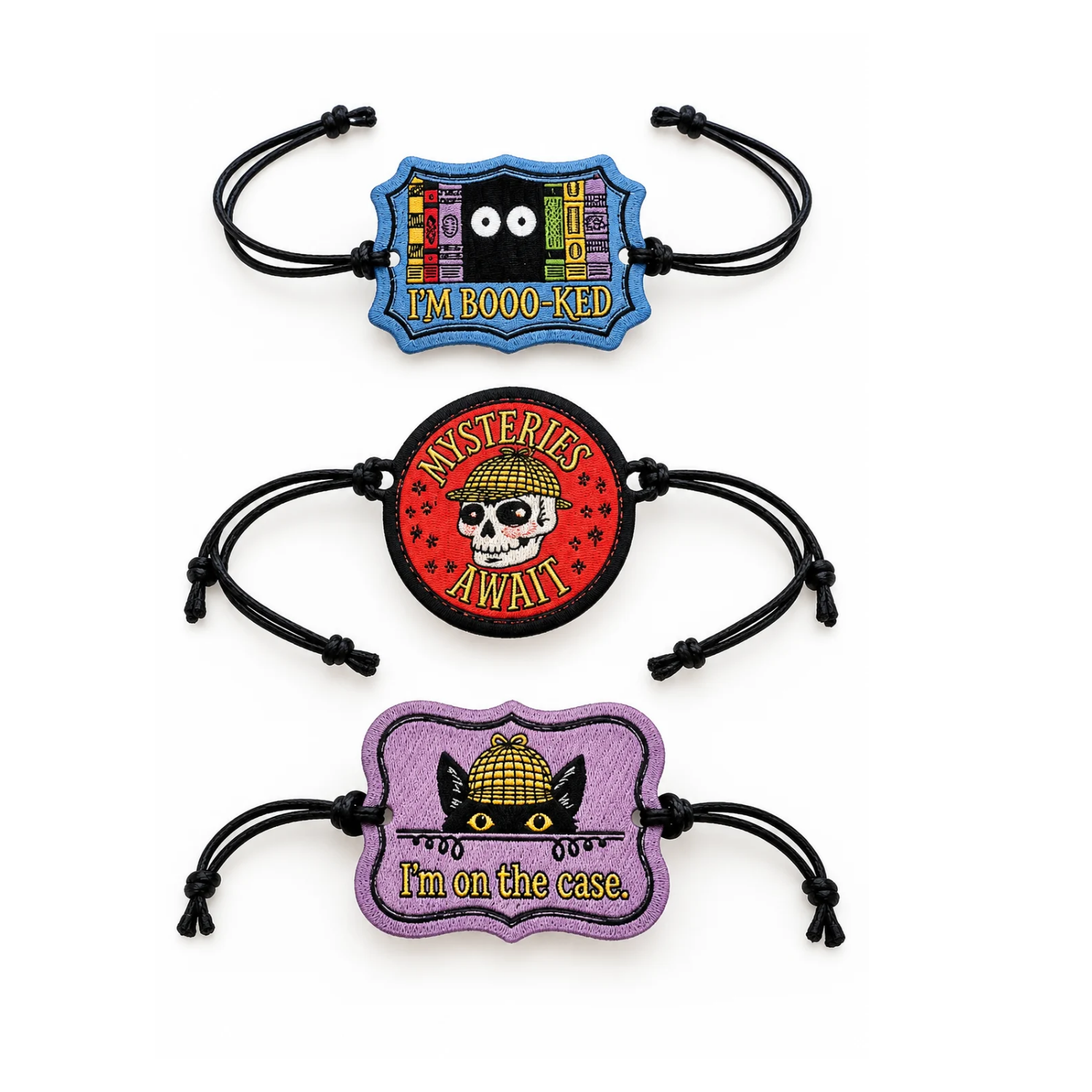 Three embroidered Mysteries Await adjustable wristbands with black cord straps on a white background. Designs include a blue “I’m Booo-ked” bookshelf with eyes, a red “Mysteries Await” detective skull, and a purple “I’m on the Case” featuring Inspector Whiskers in a yellow detective hat.