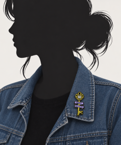 Gold "Books Hold the Key" enamel pin shaped like an ornate key with an open-book design, shown on the collar of a denim jacket