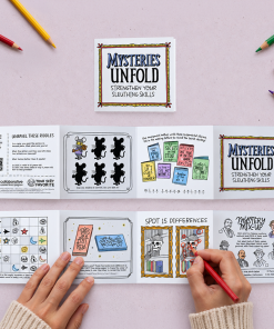 Overhead view of the 2027 “Mysteries Unfold: Strengthen Your Sleuthing Skills” accordion-style activity booklet, shown folded and fully extended on a pale lavender surface. The black-and-white puzzle pages feature riddles, a mouse shadow-matching challenge, a secret book-title puzzle, symbol grid, spot-the-differences activity, and mystery character matching game. Hands use a red colored pencil to complete a puzzle, while colorful pencils surround the booklet.