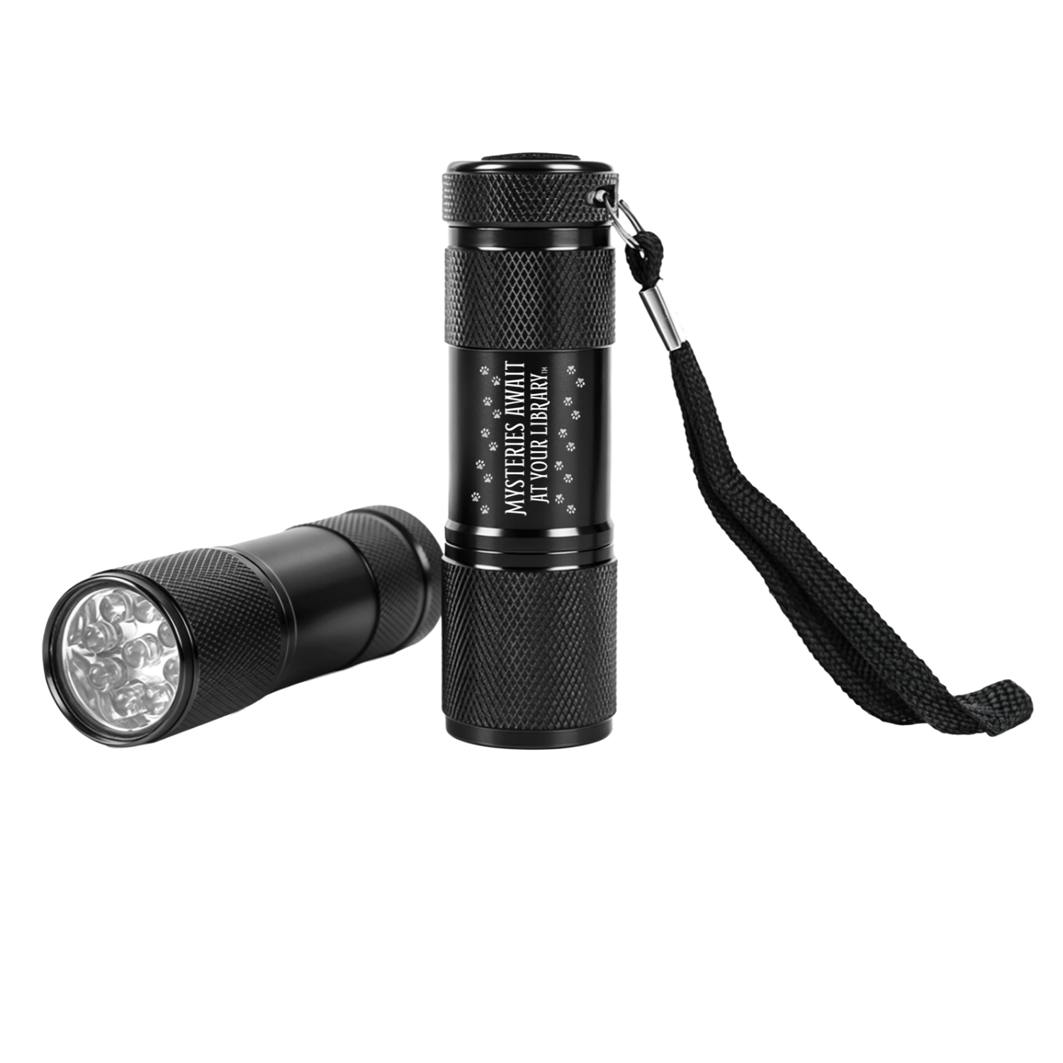 Two black mini LED flashlights with textured grips, shown upright and lying horizontally to display the LED bulbs. One features the white “Mysteries Await at Your Library” slogan with paw print accents and an attached black wrist strap.