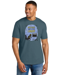 Model wearing a slate blue unisex crewneck T-shirt featuring Laurie Conley’s 2027 “Mysteries Await at Your Library” artwork. The design shows Inspector Whiskers, a black detective cat wearing a yellow hat and scarf, holding a magnifying glass beside a library book return slot. Yellow and black lettering appears against a lavender background. Model shown wearing blue jeans against a white background.