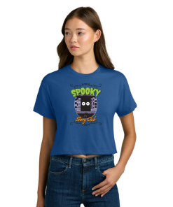 Model wearing a royal blue cropped T-shirt featuring the “Spooky Story Club” design with bright green and orange lettering and a black, wide-eyed ghostly character surrounded by bookshelves. Paired with blue jeans against a white background.